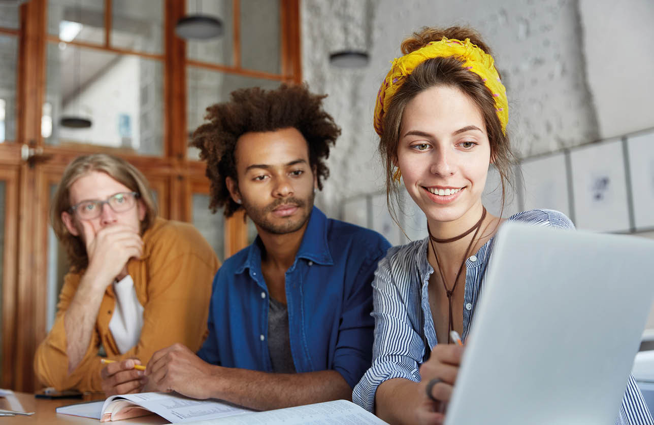 People, cooperation, teamwork and partnership. International team of coworkers using laptop computer together while working on their common project, developing business strategy and making plans