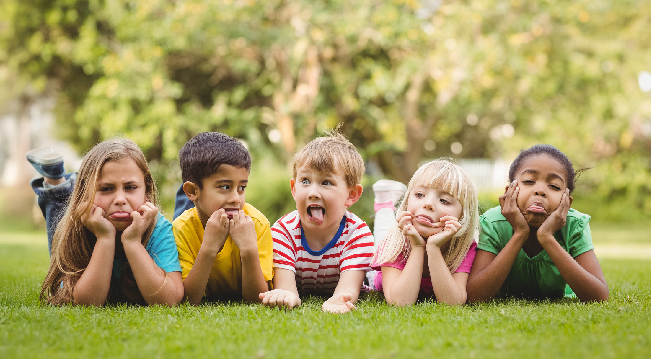 Happy classmates grimacing and lying in grass on campus