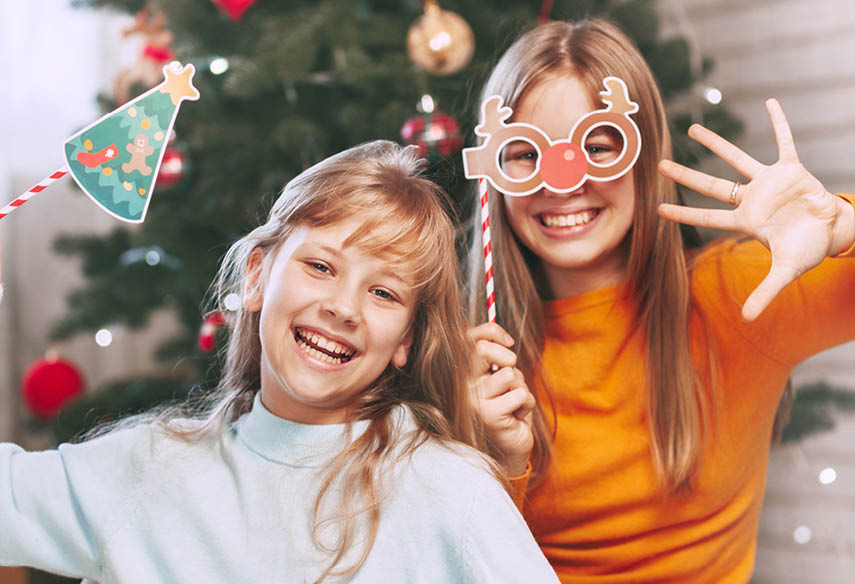 Two little blond sisters of European appearance are looking at the frame and waving their hand, communicating via a mobile tablet via video link with friends and grandparents for Christmas. Christmas greetings online. Social distancing on New Year's Eve.